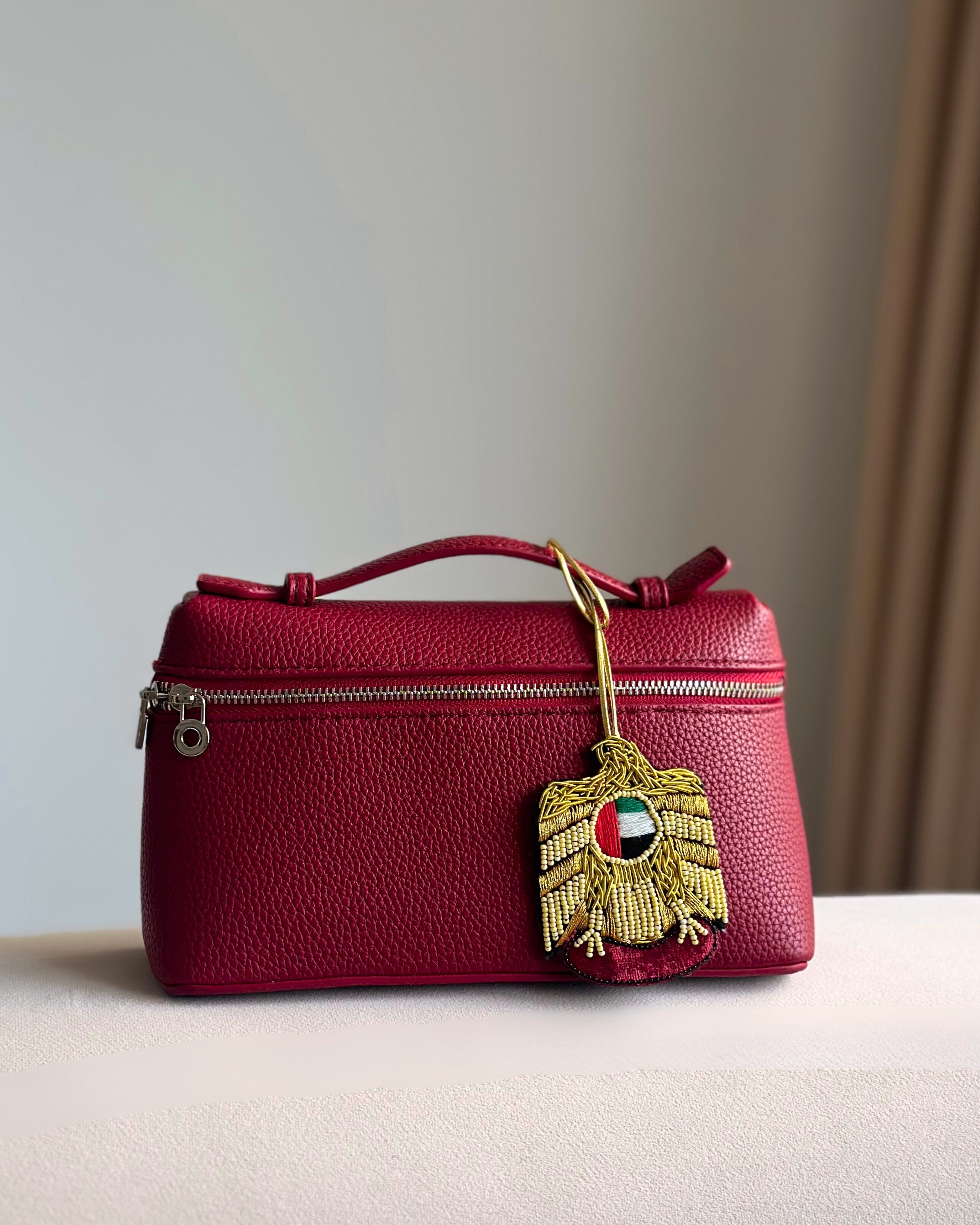 Red handbag with a gold and red decorative tag on a neutral background