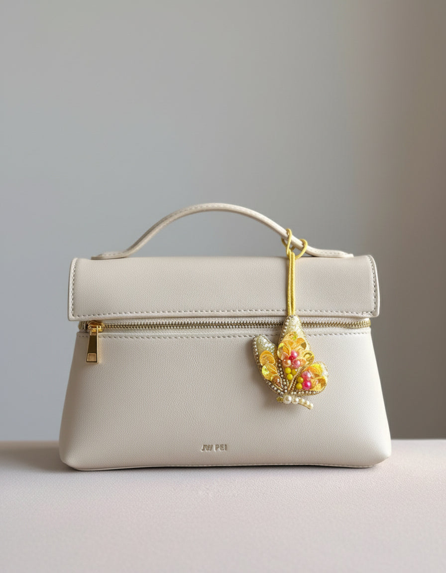 White handbag with a decorative yellow flower charm on a neutral background
