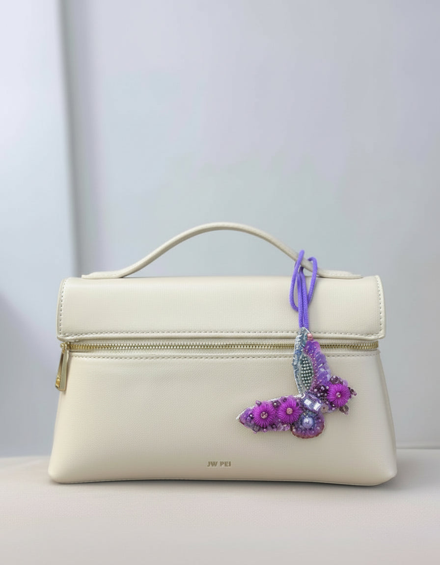 White handbag with a decorative purple charm on a light gray background